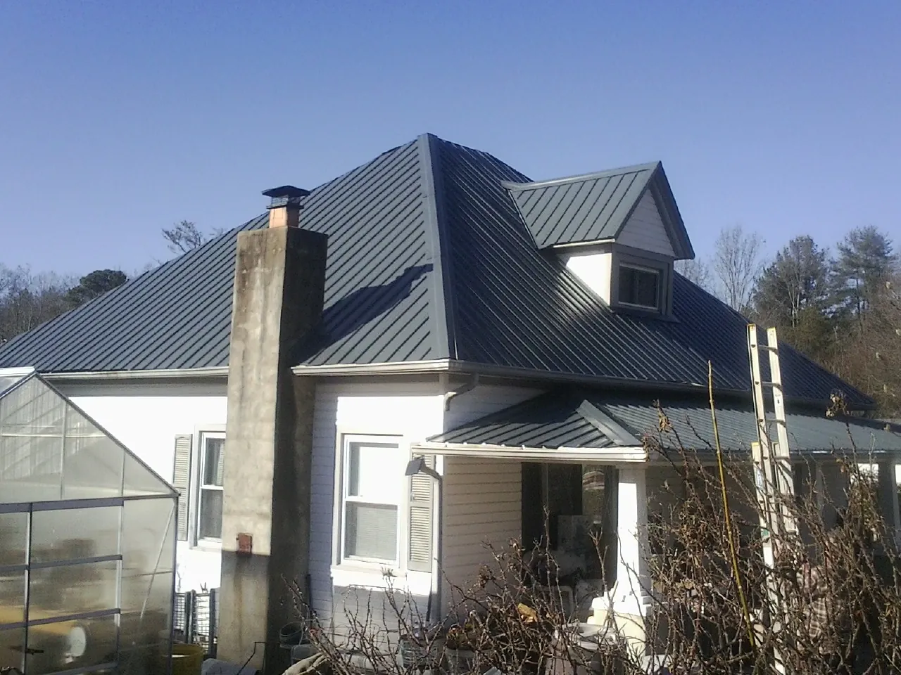 Dark blue standing seam metal roof on a white farmhouse with dormer — Slate & Tile Roof Repair by Roofing Brothers in Hosford