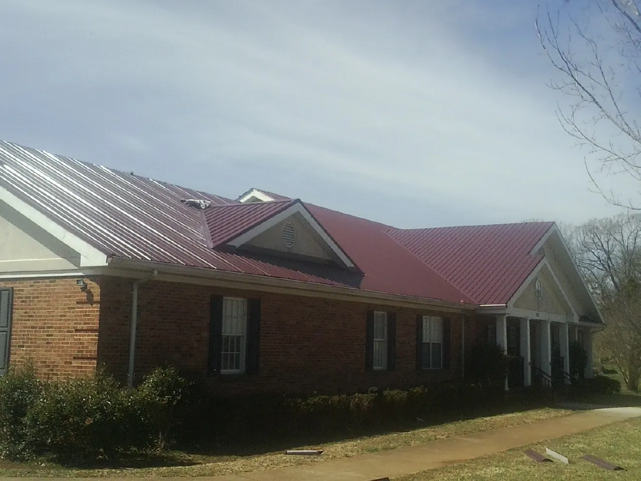 Red metal roof with gabled entries on a long brick building, from a Hail Damage Roof Repair job in Hosford
