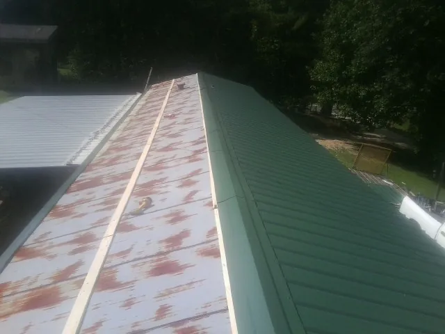 Old rusted panels beside newly installed green metal roofing — Wind Damage Roof Repair by Roofing Brothers in Hosford
