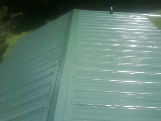 New green metal panels meeting at the ridge of a roof — Flat Roof Repair work by our crew in Hosford