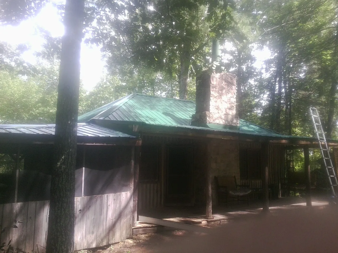 Green metal roof and stone chimney above a log cabin porch in Hosford