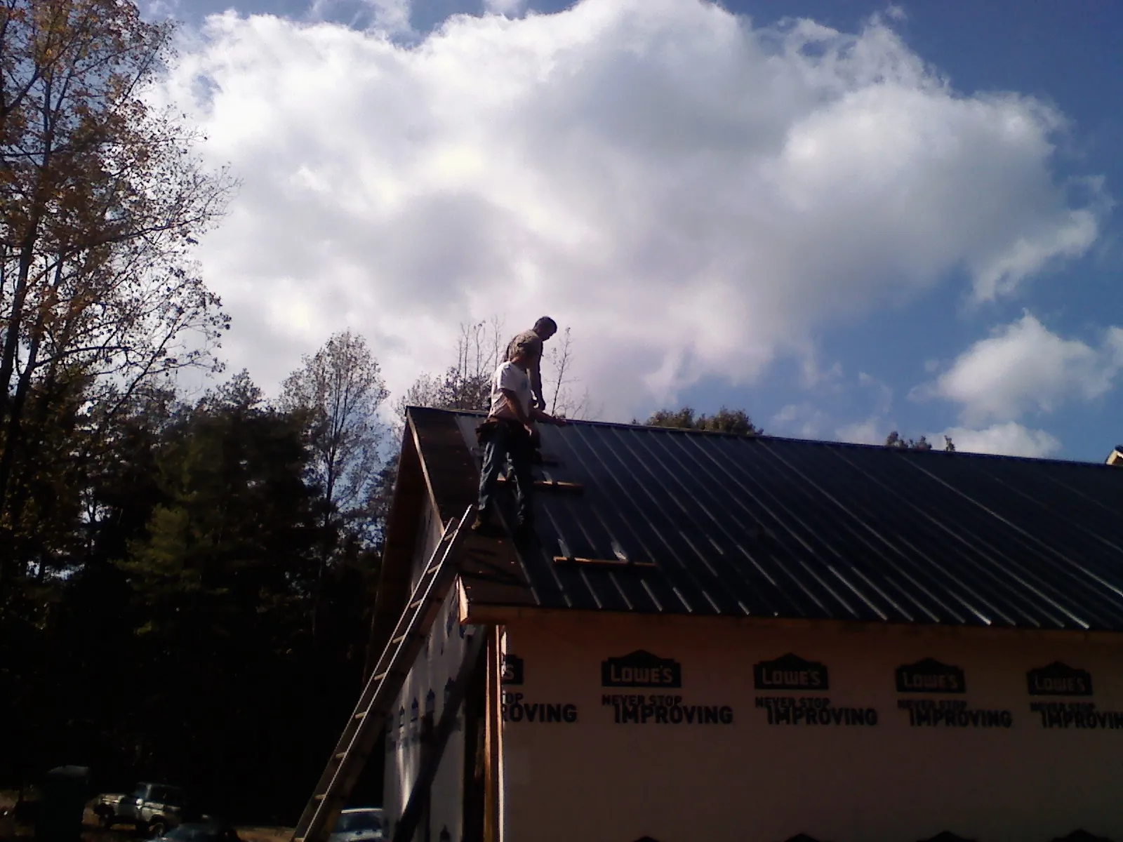 Roofer fastening dark metal panels high against a cloudy sky, from a Roof Inspection job in Hosford