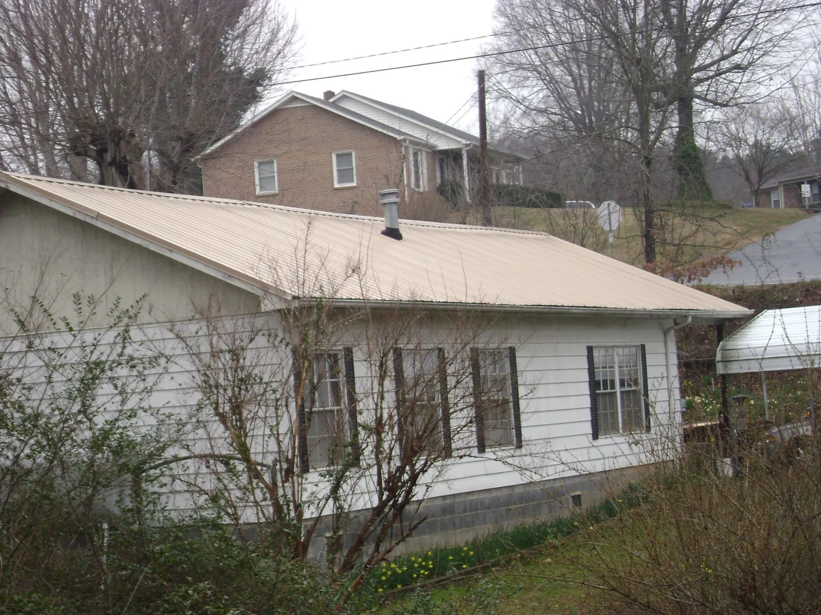 Tan metal roof on a white sided house set into a hillside — Commercial Roofing by Roofing Brothers in Hosford