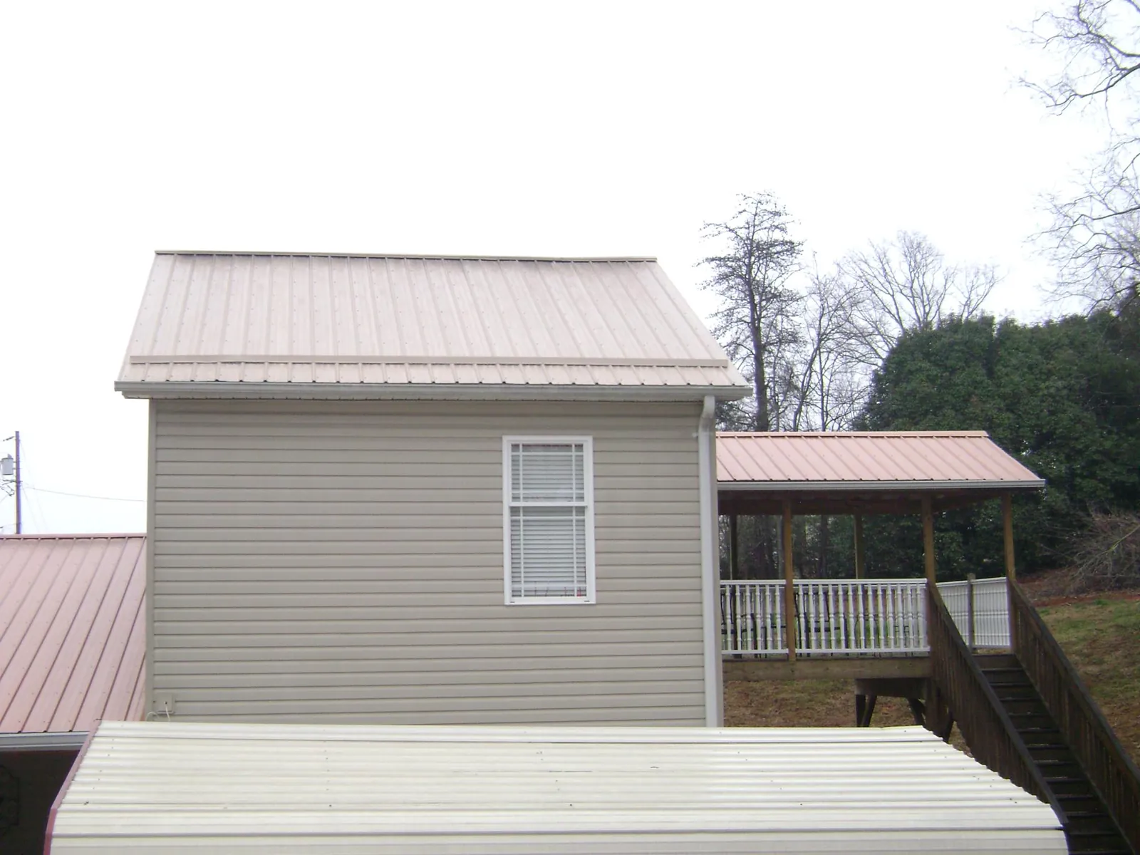 Tan metal roofs on a two story addition and attached porch, from a Roof Replacement job in Hosford